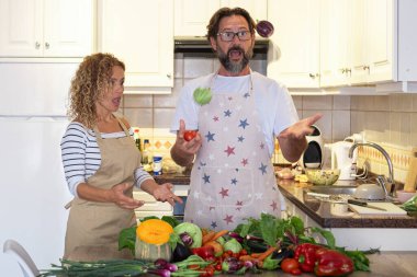 Yetişkin erkek ve kadın taze sebzelerle yemek hazırlarken mutfakta oynayıp eğleniyorlar..