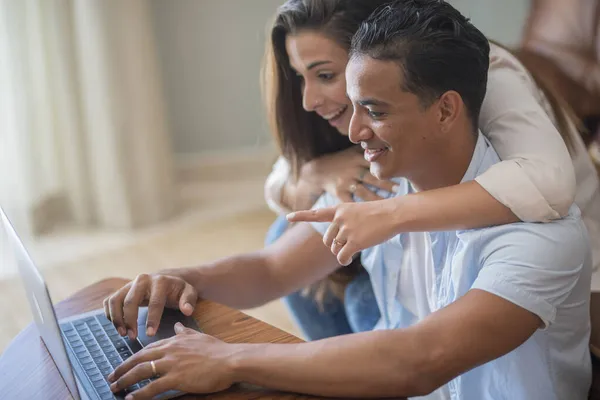 一对快乐的跨种族的现代夫妇坐在沙发上 在家里用笔记本电脑 — 图库照片