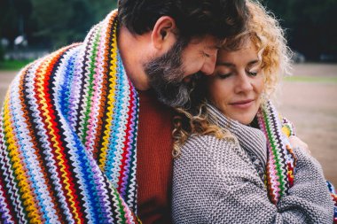 Romantik yetişkin çift, açık hava parkında yün renkli bir battaniyeyle örtülmüş duygu ve aşkla bir arada kalırlar..