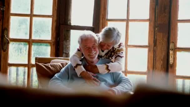 幸せとシニア白人カップル笑顔を楽しみ 居心地の良い家のキャビンシャレーで椅子に座って抱き合って — ストック動画