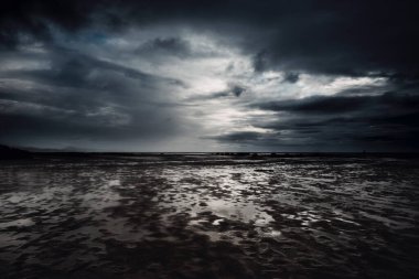 Dramatic cloudscape and flood beach in dark night weather. Stormy and rainy sky with ocean in background. Epic seascape with white sunset light and black clouds. clipart