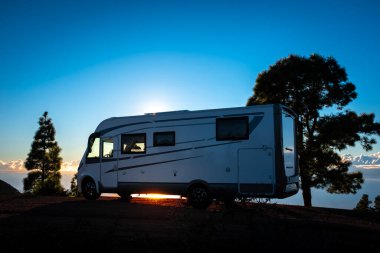 Gün batımı ışıklarına ve ağaçlara parkedilmiş bir karavan. Alternatif yaşam tarzı vanlife ve seyahat tutkusu kavramı. Kamp arabasıyla yaz tatili.