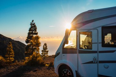 Arka planda güzel bir günbatımı ve özgürlük ve vanlife alternatif yaşam tarzının tadını çıkarmak için doğada park edilmiş modern bir karavan. Seyahat insanları aile ve turizm konsepti