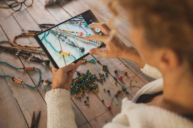 Masanın üzerinde duran boncuklu kolyede tabletle fotoğraf çeken bir kadının arka görüntüsü. Modern çevrimiçi mağaza işi kavramı