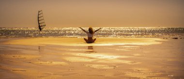 Turist ve yaz tatili insanların yaşam tarzı için afiş başlığı. Arka planda okyanus ve altın günbatımıyla kumsalda oturan keyifli ve neşe dolu dişi.