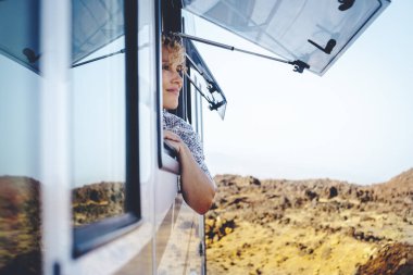 Güzel yetişkin kadın gülümseyip kamp alanında özgürlüğün tadını çıkarıyor. Kamp arabasının penceresinin önünde hayranlıkla izliyor. Yaz tatili kavramı ve özgür kadın bağımsızlık insanları
