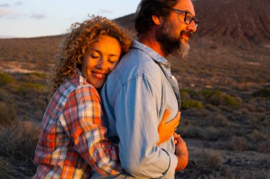Olgun genç çiftler birbirine aşık olurlar ve gün batımında romantik aktivitelerden hoşlanırlar. Erkek ve kadın birbirine sarılıyor ve birbirlerini seviyorlar. Arka planda dağlar. Seyahat kavramı