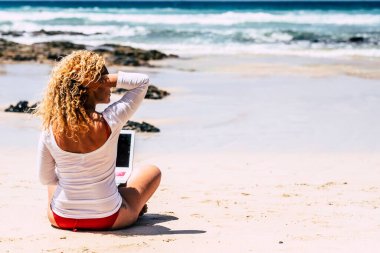  Güzel bir kadının dizüstü bilgisayarla ve kablosuz bağlantıyla plajda çalışmaktan keyif almasının arka görüntüsü. Akıllı çalışma ve uzak işçi çevrimiçi iş konsepti yaşam tarzı