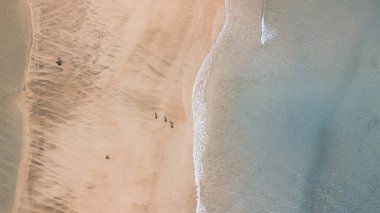 Şeffaf tropikal okyanus dalgalarıyla güzel sarı kumsal manzaralı dikey drone görüntüsü. Tatil için özgürlük ve yaz seyahati konsepti. Turistler ve turizm güneşin tadını çıkarıyor