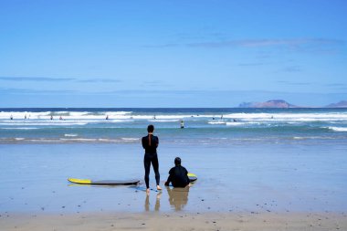 İnsanlar sahilde sörf ve su sporları yapıyor. Dalgaların tadını çıkarmaya hazır iki adamın görüntüsü. Yaz tatili ve sörf sınıfı konsepti. Arka planda mavi okyanus ve gökyüzü
