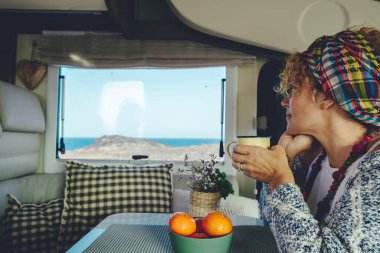 Dişi turist sakin bir karavanda oturup pencereden dışarıdaki güzel doğayı seyrediyor. Seyahat aracı konsept yaşam tarzı. Van Life kadın insanları