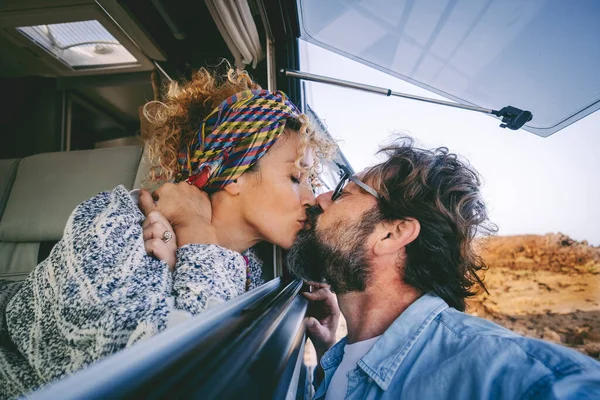 Young adult couple in love kissing and enjoying travel vacation lifestyle together. Woman kissing man through the window in camper car. Tourist and van life modern alternative concept life. Relationship