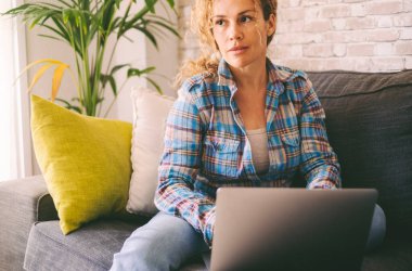 Huzurlu ve kendinden emin yetişkin kadın portresi modern dizüstü bilgisayarda çalışıyor. Oturan kadınlar kapalı alandaki teknolojik aktivitelerden zevk alırlar. Sosyal medya ve online iş konsepti yaşam tarzı