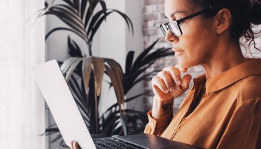 Okuyan ve dizüstü bilgisayar kullanan kadınların yan görüntüsü. Evde çalışmak zekiceydi. İnternette çalışan yetişkin bir kadın. Çevrimiçi bağlantı yaşam tarzına sahip modern yaşam tarzı insanlar