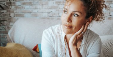 Huzurlu ve rahat bir yetişkin kadının portresi kanepede oturuyor. Kendine güvenen ve mutlu gülümseyen kadınlar. Sağlıklı bir kadın yüzüne dokunuyor ve düşünüyor.