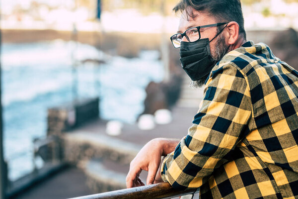 Worried man wearing protection mask for coronavirus covid-19 emergency in outdoor leisure activity alone. Adult mature male people with medical protection black mas looking and thinking
