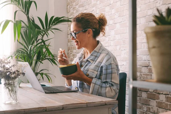 Vista Lateral Mujer Joven Adulta Sonriendo Comiendo Ordenador Portátil Escritorio — Foto de Stock