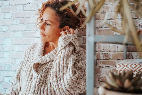 Side view portrait of adult attractive lady with serious and thoughtful expression at home against a brick wall. Female people and personal problems. Sadness and bad lifestyle concept
