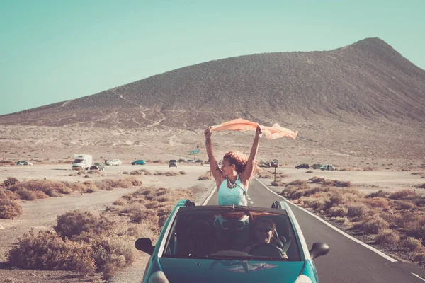 Travel and friendship concept lifestyle. Adult woman overjoyed staying outside the roof of a convertible car while her friend drive smiling. Concept of summer holiday vacation and road trip