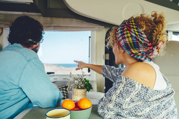 Back view of happy couple admiring the beach inside a modern camper van alternative tourist house. Travel and summer holiday vacation with rent caravan. Van life and freedom people enjoying adventure