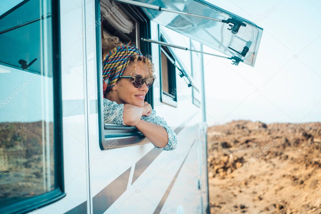 Happy young attractive woman admire and enjoy the view from modern camper van window. Alternative home and travel lifestyle people. Van life. Summer holiday vacation on vehicle. Free female smile