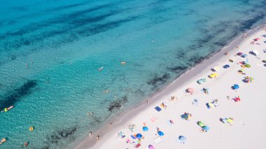 Okyanus tatilinin tadını çıkaran turistlerle dolu yaz plajının havadan görüntüsü. Seyahat kavramı ve inanılmaz varış yeri, beyaz kum ve mavi okyanus suyu, mutlu güneşlenen insanlardan oluşan gruplar. Drone görünümü