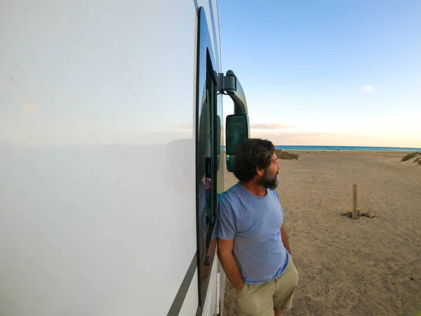 Mature man standing outside a modern camper van admiring the ocean and enjoying the beach. travel people lifestyle concept. Freedom camp site. Adult looking horizon and nature