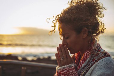 Meditasyon ve iç denge mutluluk konsepti. Dua eden ve dışarıda meditasyon yapan genç bir kadının yan portresi. Arka planda günbatımı okyanusu var. Ruh sağlığı yaşam tarzı kavramı