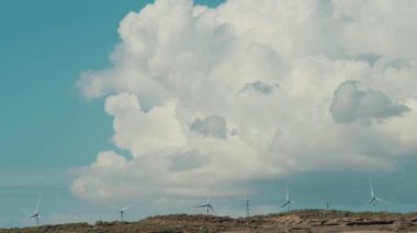 Kırsal kesimdeki rüzgâr türbinleri bulutlu mavi gökyüzüne karşı. Yeşil enerji üretimi kavramı ve iyi bir gelecek çevre yaşam tarzı. Rüzgar değirmenli yenilenebilir elektrik çiftliği