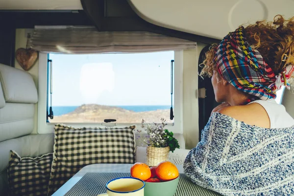 Back view of a woman looking outside the window inside a camper van. Van life and off grid lifestyle concept. Female people enjoying view outdoor . Traveler and holiday vacation. Nomadic life tourist