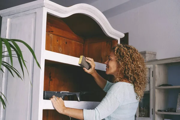 Evde eski yenilenmiş mobilyalar üzerinde çalışan yetişkin bir kadın. Sürdürülebilirlik yaşam tarzı ve geri dönüştürülmüş dairesel pazar ürünleri kavramı. Evde hobisi olan mutlu kadın aktiviteleri.