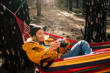 Fotoğraf makineli genç bir kadın seyahat etmekten zevk alıyor vahşi ormandaki hamakta uzanıyor. Parktaki neşeli kadın insanlar alternatif macera tatilinde yalnızlar.