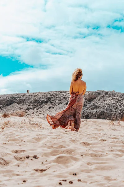 站着的女人 穿着雅致的连衣裙 站在荒山野岭前 蓝蓝的天空中点缀着云彩 旅行和宁静的生活方式 裸体的女性赤脚在沙滩上行走 — 图库照片