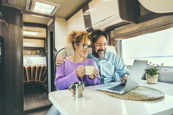 Modern couple use together laptop inside camper van. Computer leisure people surfing the web. Traveler planning next destination smiling and enjoying freedom living off grid. Digital nomad concept