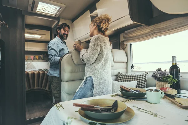 Happy adult couple enjoy vacation on camper van and prepare lunch together. Alternative travel lifestyle for modern people. Man and woman smile inside motor home. Van life and holiday trip vacation