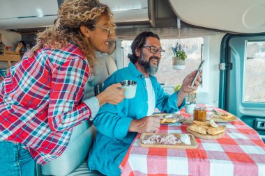 Telefondaki uygulamayı göster ve modern bir karavanın içindeki bir kadına bir sonraki yolculuk için plan yap. Seyahat ve tatil tatili ya da minibüs yaşam tarzı kavramı. Alternatif boş zamanlardaki insanlar.