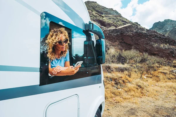 One independent woman using the phone outside the window of her alternative home camper van. People and travel destination with camper van vehicle. On the road holiday vacation and freedom lifestyle