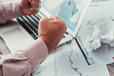Kağıt ve bilgisayar ekranındaki insan yumruklarını grafiklere yaklaştır. Borsa opsiyonları ve kötü ekonomi haberleri kavramı. Kriz ve iş aktiviteleri. Tüccarlar stres ve çaresizlik
