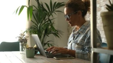 Laptopta çalışan beyaz bir kadın arka planda yeşil bitkilerle masada oturuyor. Modern insanlar ve çevrimiçi ecommerce mağaza yönetimi kavramı. Bilgisayarda güzel bir kadın sohbeti.
