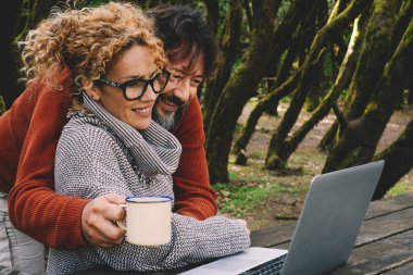 Erkek doğa parkında dizüstü bilgisayar kullanırken kadına sarılıyor. Dijital online seyahat aktivitelerinde bilgisayar izleyen çift kavramı. İnsanlar ve modern çalışma aktiviteleri