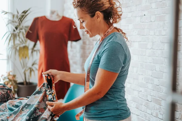 Woman in tailor activity at home or design studio store. Workshop of tailoring. Adult female working with textile and mannequin in background. Stylist lady creating clothes and enjoy hobby indoor