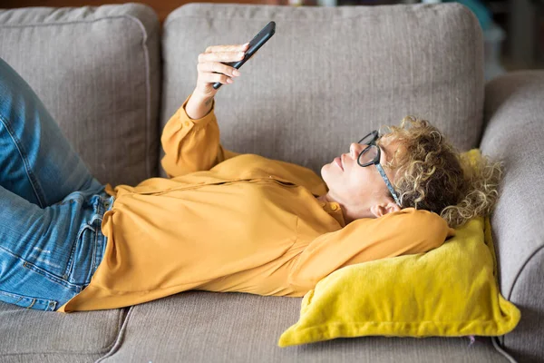 Woman with yellow shirt enjoy time and leisure at home laying on the sofa and using mobile phone connection, People and technology. Modern lady communicate and use social media account and web page