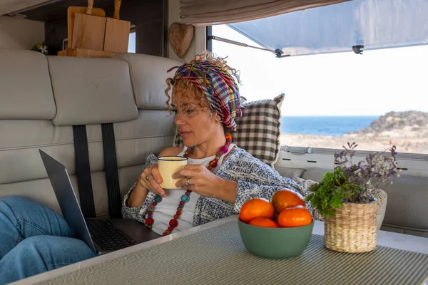 One independent woman laying and working inside a camper van with laptop and connection. Free lifestyle and alternative office workstation for modern online worker people. Digital nomad lady activity