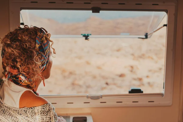 Back view of traveler woman looking outside the camper van window. Van life and travel people lifestyle. Freedom living off grid in a vehicle and alternative house on wheels. Concept of life