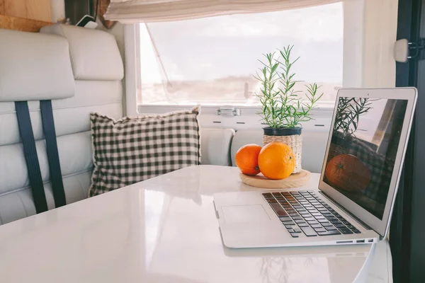 Interior view of modern camper van vehicle with empty elegant white table and laptop on it. Concept of vacation and home to live van life off grid. Workplace unusual office and freedom concept