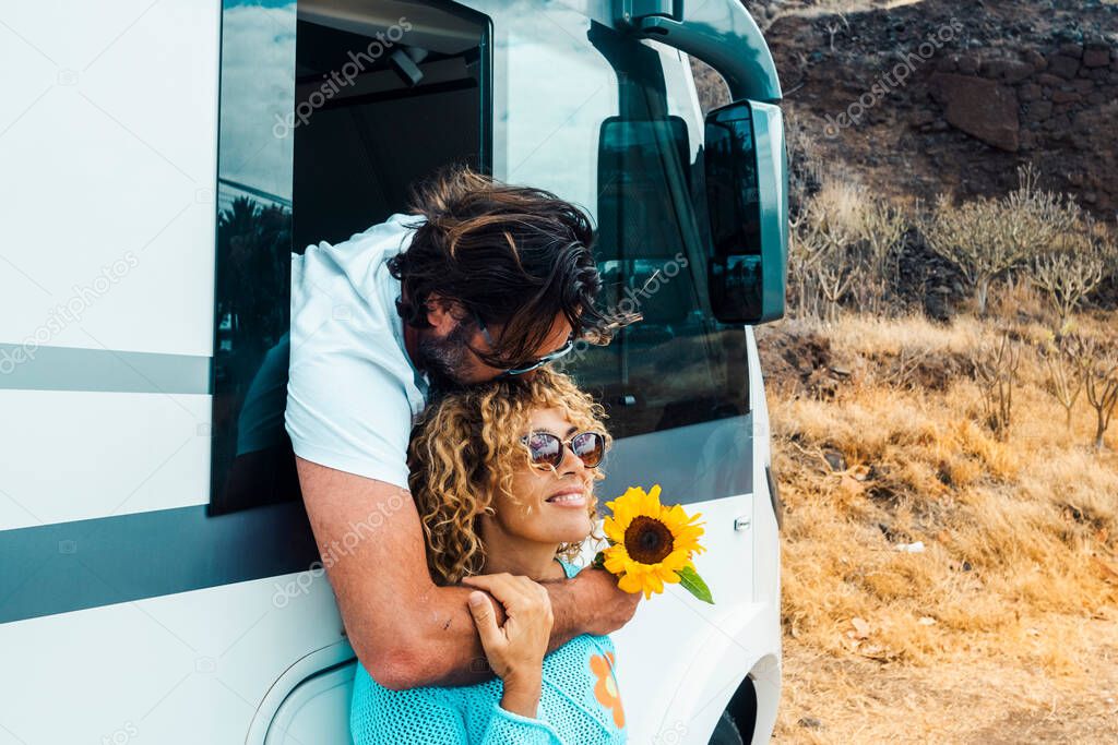 Man kissing woman and both enjoy travel lifestyle. Happy couple hug and smile in relationship against a modern camper van motor home. Alternative vacation on the road and freedom off grid life