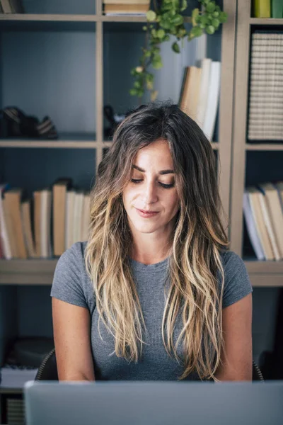 Modern millennial young woman work on computer at the desk in home office alternative business workstation. Female smile and watch pc display. Freelance digital nomad and smart working concept life