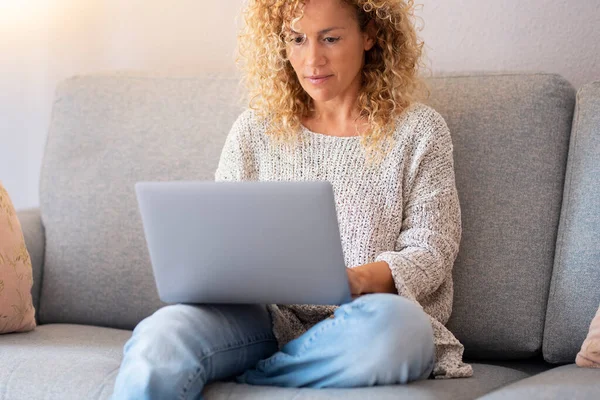 Busy woman working on laptop at home sitting on the sofa. Alternative office workplace and female people using computer and having leisure relax activity indoor. Modern job and connection concept