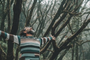 Doğa aşığı yaşam tarzı. Mutlu turistler kollarını açıp dışarıda parkın tadını çıkarıyorlar. Arka planda yeşil orman ormanı olan kollarını uzatan bir adam. Seyahat yeri.