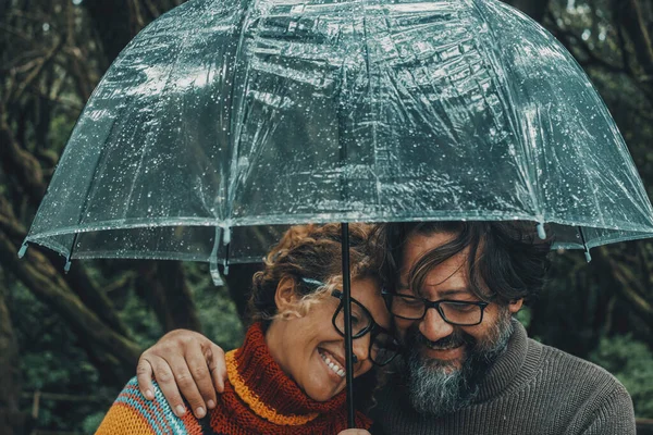 Romantic couple in love under umbrella in rainy day. Man and woman enjoy relationship and happiness together in winter autumn rain. Romance and people smiling and hugging at the park in leisure moment